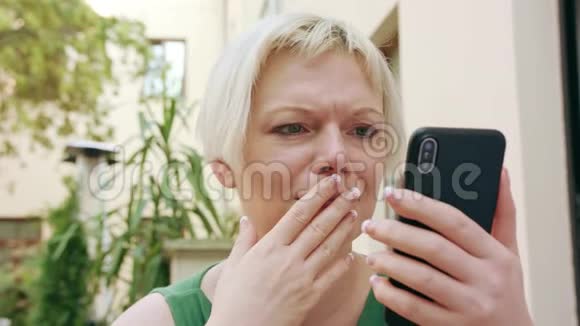 年轻的金发女人坐在外面用电话视频的预览图