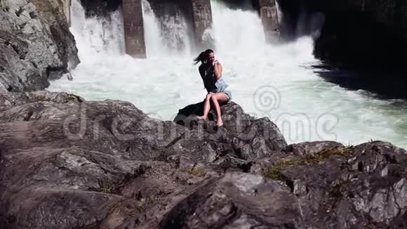 坐在岩石上的漂亮女孩在瀑布后面视频的预览图