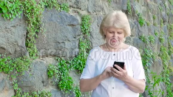 使用带有耳机的智能手机的老年妇女背景中野生石头的复古墙视频的预览图