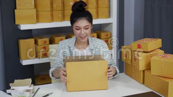 女在线企业家用胶带在家庭办公室包装包裹盒准备产品交付给客户视频的预览图