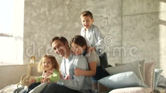 三个孩子和一个年轻的父亲拥抱坐在床上家人的早晨快乐的父亲父亲节视频的预览图