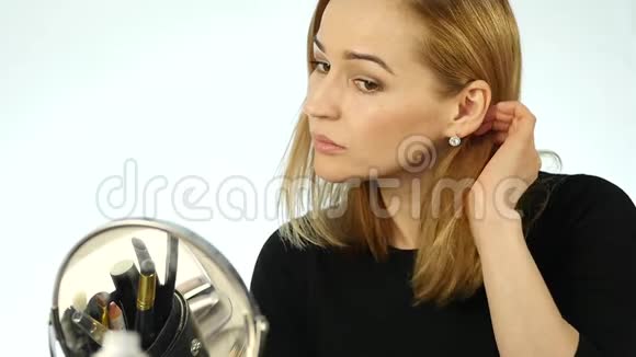 年轻的金发女人站在家里的镜子前纠正她的头发慢动作视频的预览图