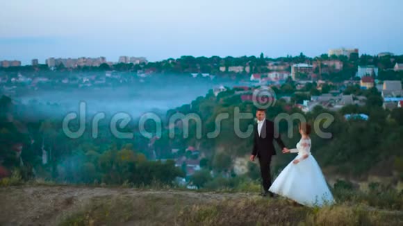 在雾和城市4k的背景下一对年轻夫妇在一片山地草地上相爱视频的预览图
