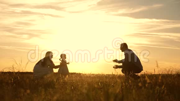 爸爸妈妈和孩子在公园里玩日落孩子迈出第一步幸福的家庭玩他们的女儿视频的预览图