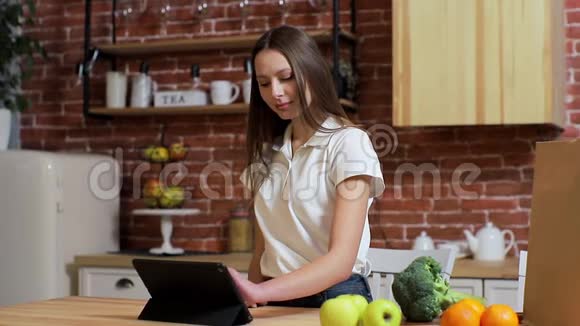 女人在家厨房的平板电脑上浏览年轻女子在平板电脑上浏览微笑着快乐视频的预览图