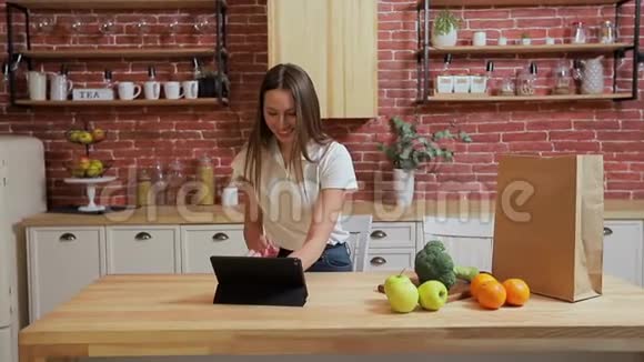 女人在家厨房的平板电脑上浏览年轻女子在平板电脑上浏览微笑着快乐视频的预览图