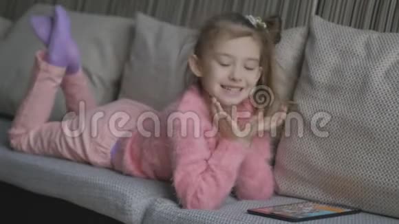 漂亮的小女孩躺在沙发上用平板电脑小孩子在家里的橙色沙发上玩笔记本电脑一点点视频的预览图