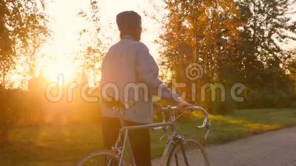 年轻的时髦女孩走在公园里背景是老式自行车和金色的城市日落4K慢动作视频的预览图