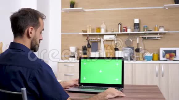 厨房里桌子上的男人看着笔记本电脑视频的预览图