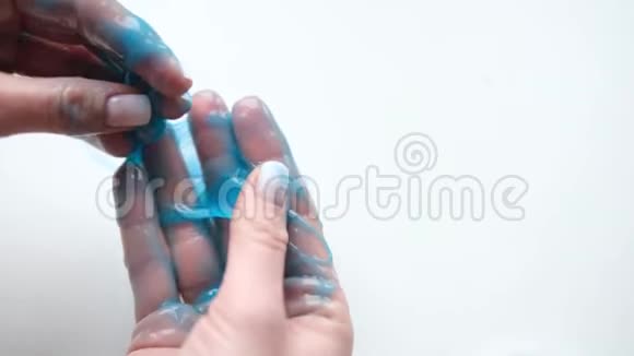 女孩把蓝色的黏液伸到两边女人的手在玩黏液玩具在白色上做黏液时髦的液体玩具棒视频的预览图