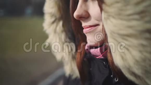 户外一位年轻美丽的红发女子的特写肖像穿着温暖蓬松夹克的女孩视频的预览图