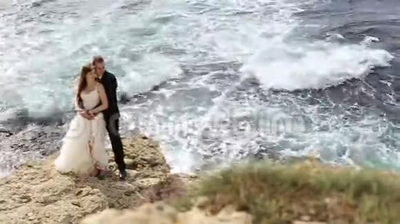 新娘和新郎在海洋上方的悬崖上视频的预览图
