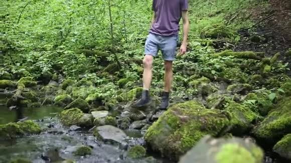 在绿色森林中穿过小溪的年轻人特写镜头视频的预览图