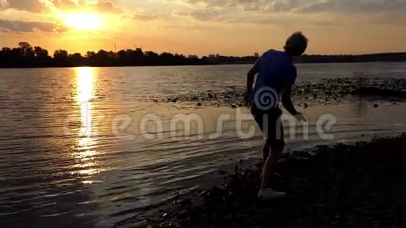 在日落的河岸上站着一个活泼的人他扔石头视频的预览图