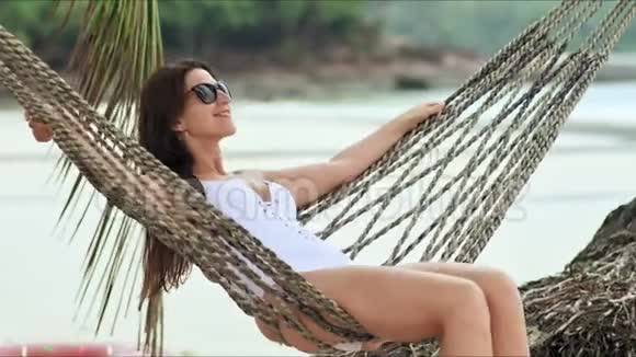 戴太阳镜的年轻美女在热带海滩的吊床上放松视频的预览图