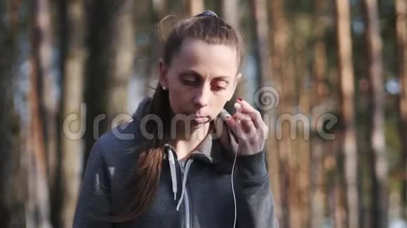 年轻女子在树林里听智能手机上的音乐视频的预览图