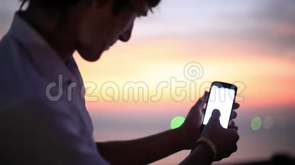 人类在日落海滩海边使用移动智能手机有模糊的bokeh灯1920x1080视频的预览图