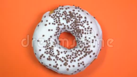 明亮和白色釉面甜甜圈与巧克力球宏观拍摄旋转的橙色背景视频的预览图