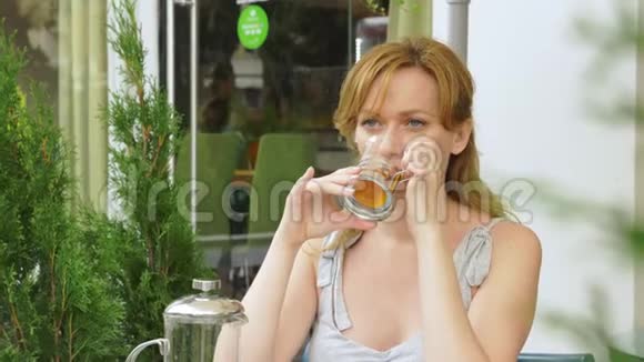 那个女孩正在喝茶坐在一家夏季咖啡馆里透明玻璃视频的预览图