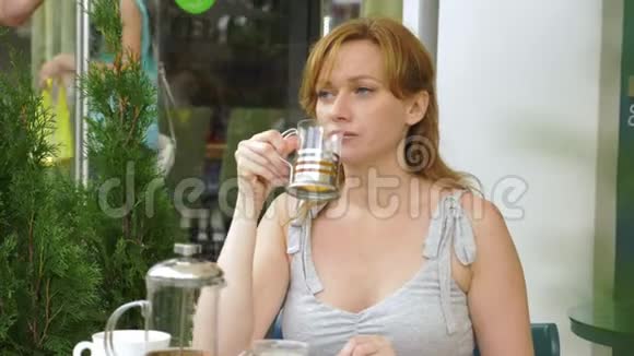 那个女孩正在喝茶坐在夏天的咖啡馆里透明玻璃视频的预览图