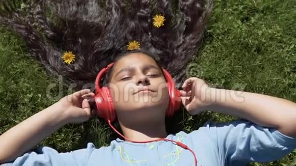 一个长发女孩躺在公园的草地上用耳机听音乐慢动作高清高清视频的预览图
