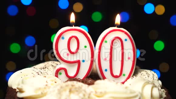在蛋糕上的90号90岁生日蜡烛燃烧在最后吹灭彩色模糊背景视频的预览图