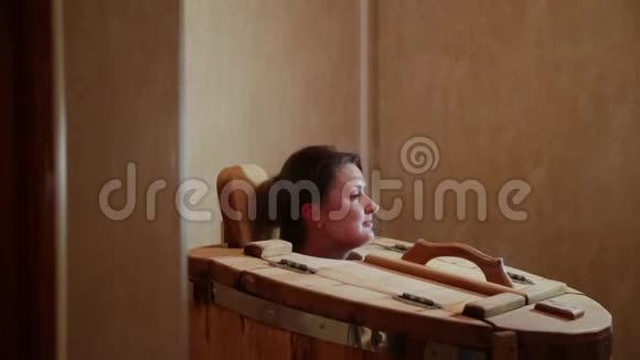 一家温泉沙龙里的雪松桶里冒出一个女人的头金发女人通过蒸汽程序恢复视频的预览图