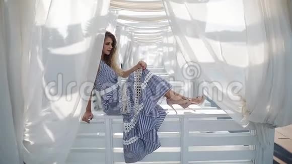 年轻漂亮的模特穿着条纹鸡尾酒连衣裙在豪华酒店度假胜地的露台上放松双手分开摆姿势视频的预览图