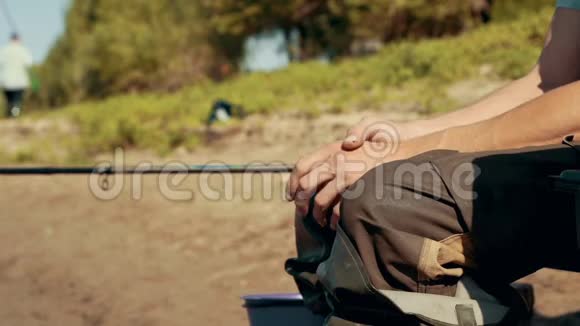 渔夫双手坐在河边的椅子上近处的钓竿在等待着咬人视频的预览图