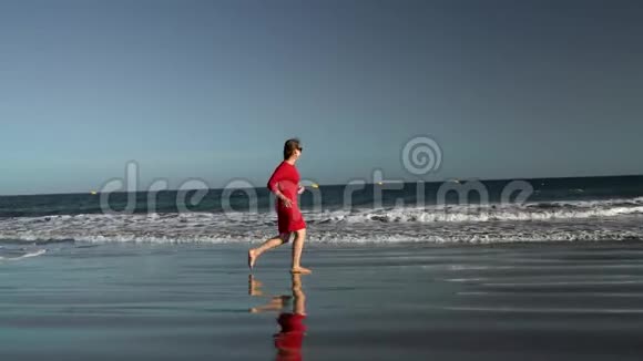 日落时分穿着红色裙子的快乐年轻女子沿着海边奔跑无忧无虑的现代生活理念慢动作视频的预览图