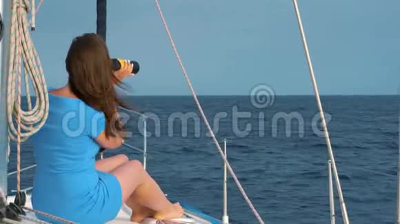穿着蓝色裙子的女人坐在游艇上用望远镜探索地平线视频的预览图