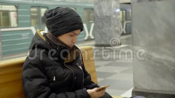 一个15岁的年轻人坐在地铁的长凳上拿着一部智能手机视频的预览图