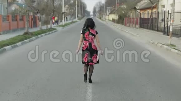 漂亮的年轻女子穿着一件带着鲜花走在公路上视频的预览图