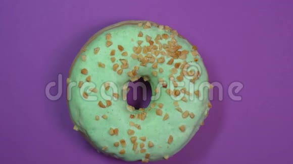 明亮的绿色釉面甜甜圈与坚果特写宏观拍摄旋转的紫色背景视频的预览图