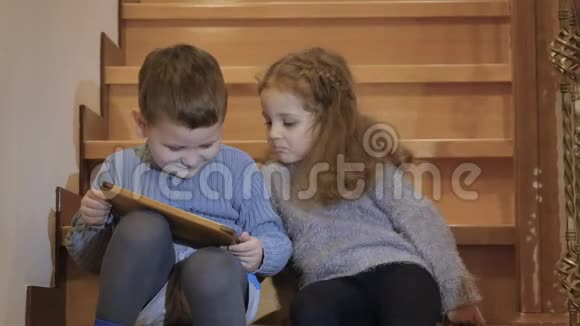 可爱的孩子们坐在楼梯上玩平板电脑视频的预览图
