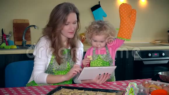 妈妈带着可爱的小女儿在平板电脑上学习饼干配方视频的预览图