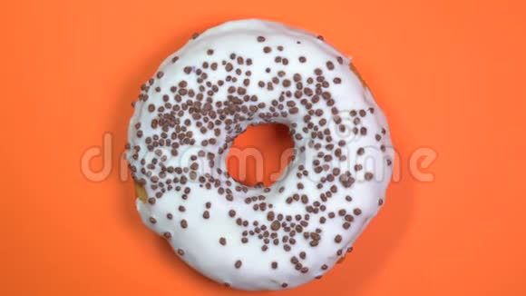 明亮和白色釉面甜甜圈与巧克力球宏观拍摄旋转的橙色背景视频的预览图