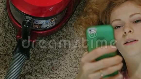 快乐的年轻女性或家庭主妇用吸尘器躺在半头手机上用手机听音乐视频的预览图