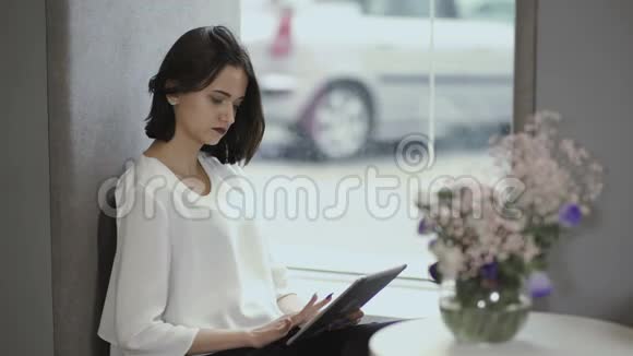 年轻女孩用平板电脑坐在窗台上视频的预览图