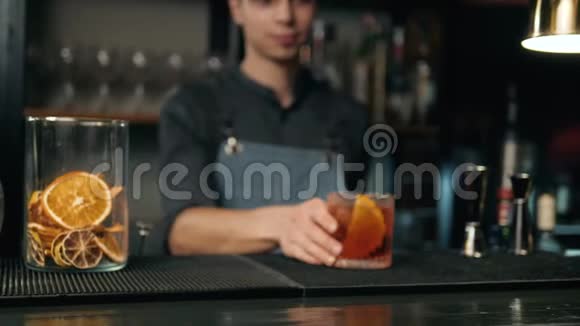把酒保的手和葡萄柚一起准备黑色鸡尾酒他正在把柚子皮放进里面视频的预览图
