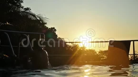 年轻人在日落时跳进游泳池的水中穿过太阳有镜头耀斑效应慢动作1920x1080视频的预览图