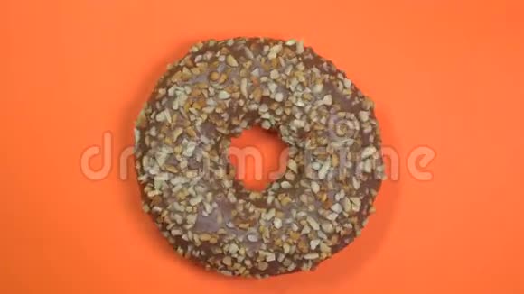 明亮而多彩的巧克力甜甜圈与坚果特写宏观拍摄旋转的橙色背景视频的预览图