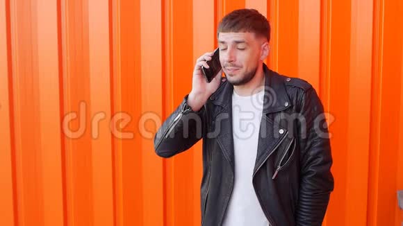 年轻的白种人穿着黑色夹克在橙色背景下打电话动作缓慢时尚视频的预览图