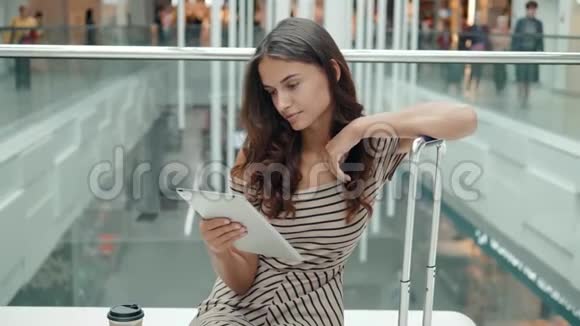 美丽的女性游客快乐的黑发女孩在机场购物中心用信用卡和平板电脑在线购物视频的预览图