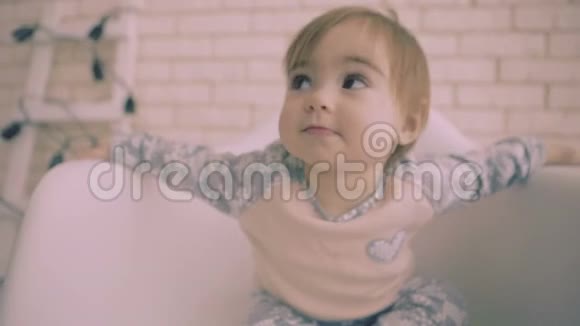 活泼开朗的小黑头发的女婴坐在白色的椅子上微笑着慢动作视频的预览图