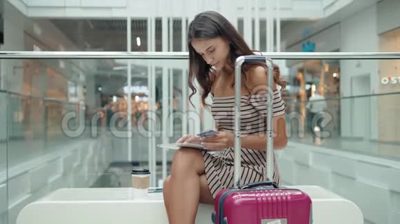美丽的女性游客快乐的黑发女孩在机场购物中心用信用卡和平板电脑在线购物视频的预览图