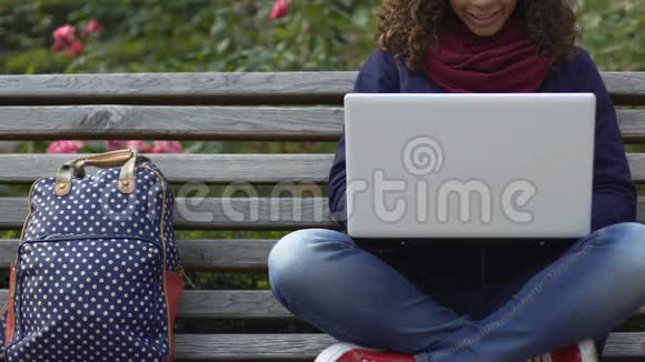 年轻的混血女学生在公园用笔记本电脑和朋友聊天视频的预览图