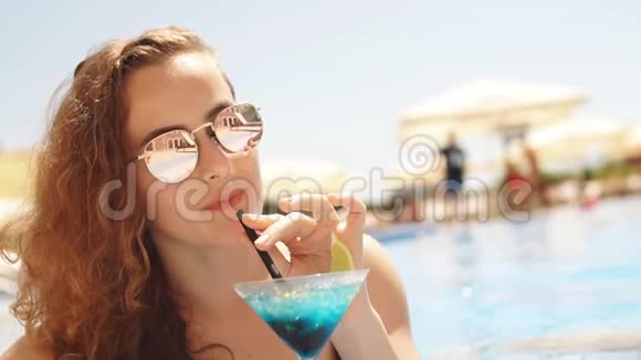 美丽的长发女人在游泳池附近放松与鸡尾酒慢动作视频的预览图