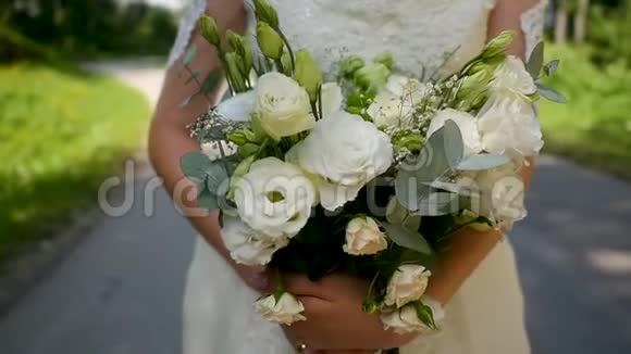 美丽的年轻新娘穿着婚纱看着手里的花和他在阳光明媚的公园里玩视频的预览图