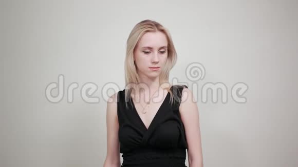 一个穿着黑色裙子的金发女孩在一个与世隔绝的白色背景下表现出情感视频的预览图